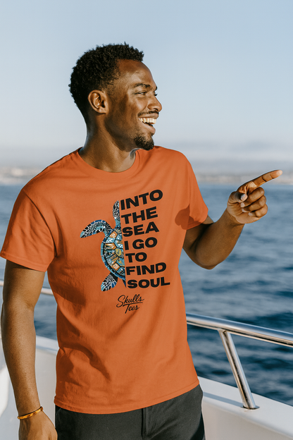 Man wearing an orange t-shirt with a turtle graphic and text, standing on a boat with ocean in the background.